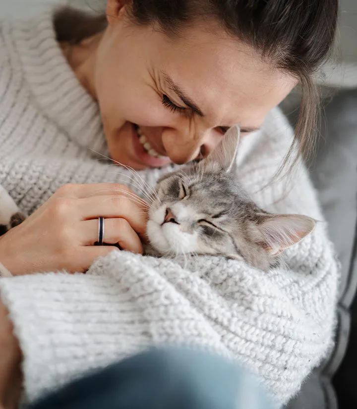 woman smiling while holding and petting striped tabby cat